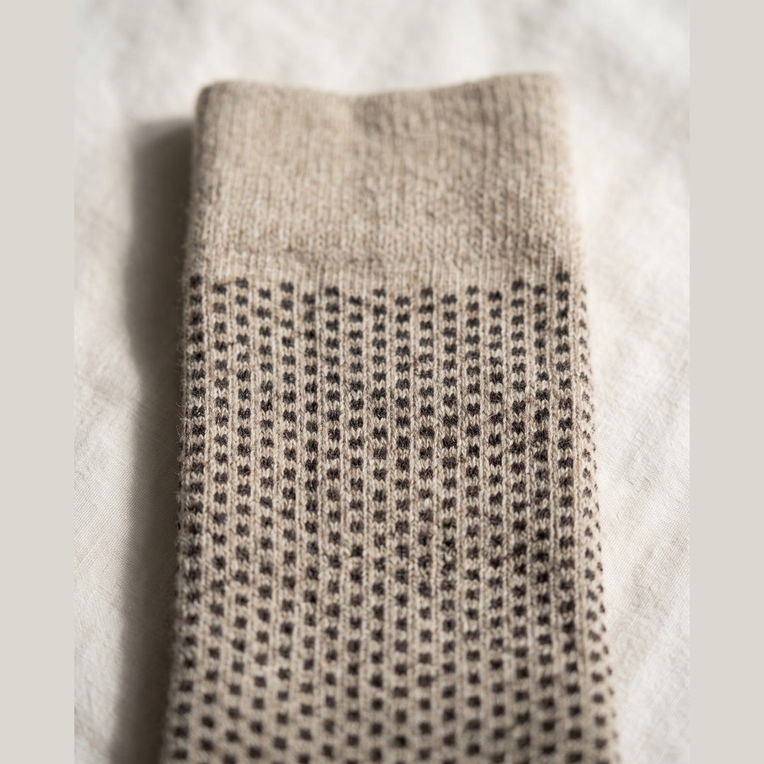 Close-up of beige birdseye lambswool sock showing the fine dot knit texture and plain cuff