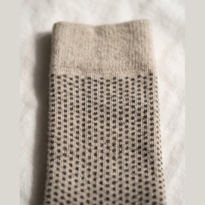 Close-up of beige birdseye lambswool sock showing the fine dot knit texture and plain cuff