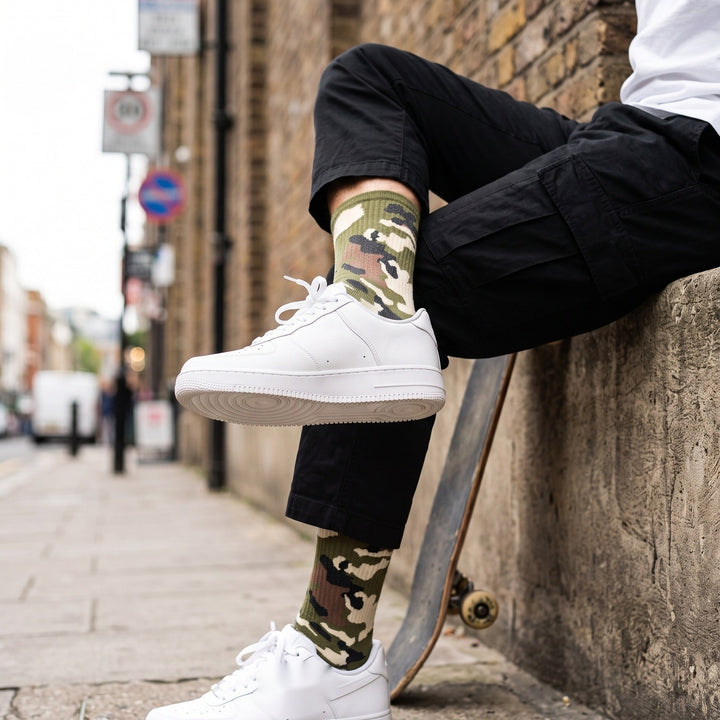 Man on a city street with a skateboard wearing green camo cushioned socks with black cargo trousers and white sneakers