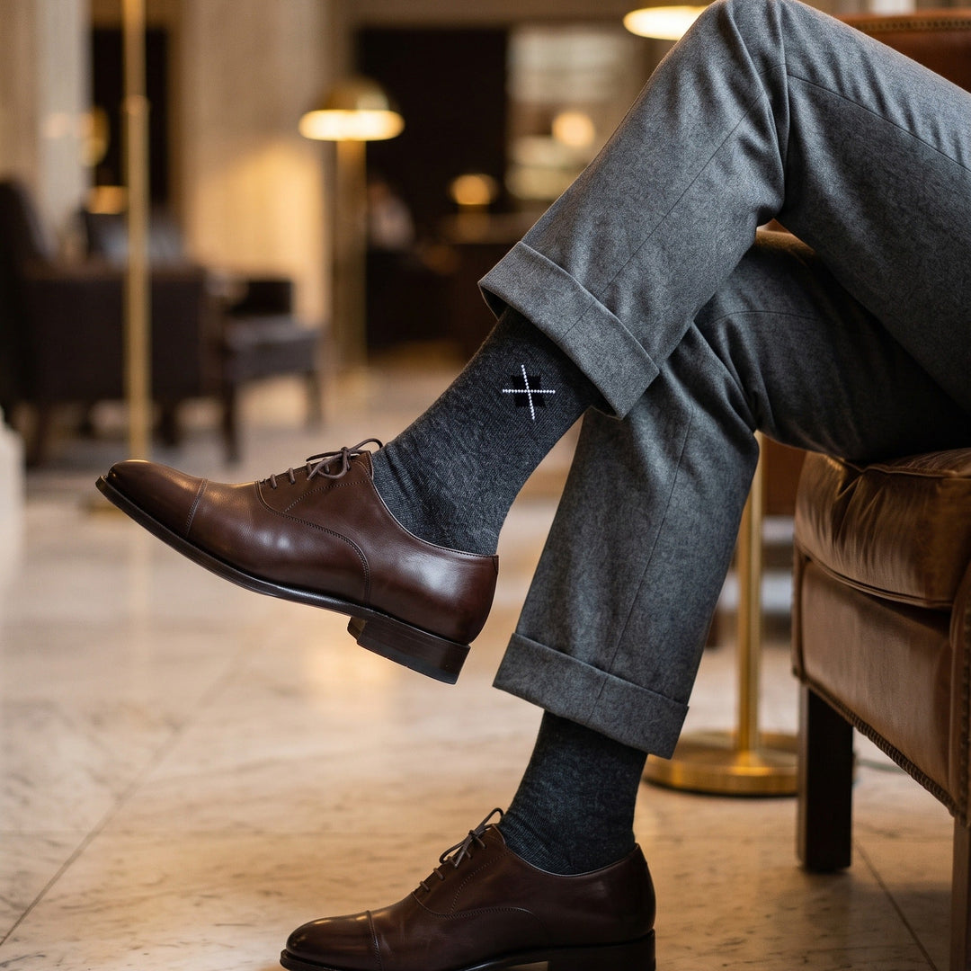 Man in a hotel lobby armchair wearing charcoal diamond stitch lambswool socks with grey trousers and brown oxford shoes