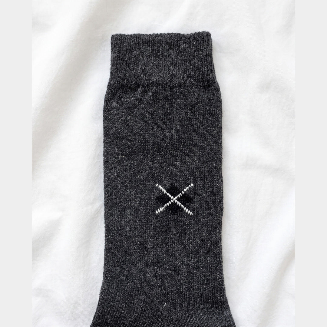 Close-up of charcoal lambswool sock showing the embroidered black diamond with white cross-stitch and ribbed cuff
