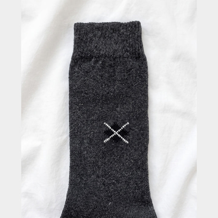 Close-up of charcoal lambswool sock showing the embroidered black diamond with white cross-stitch and ribbed cuff