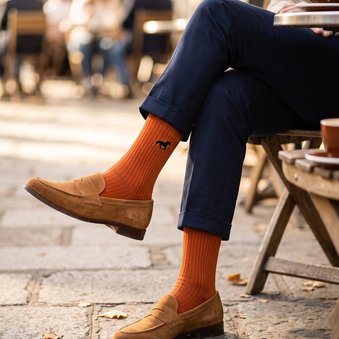 Man wearing burnt orange Galloper ribbed crew socks with embroidered horse, tan loafers and navy chinos at a café