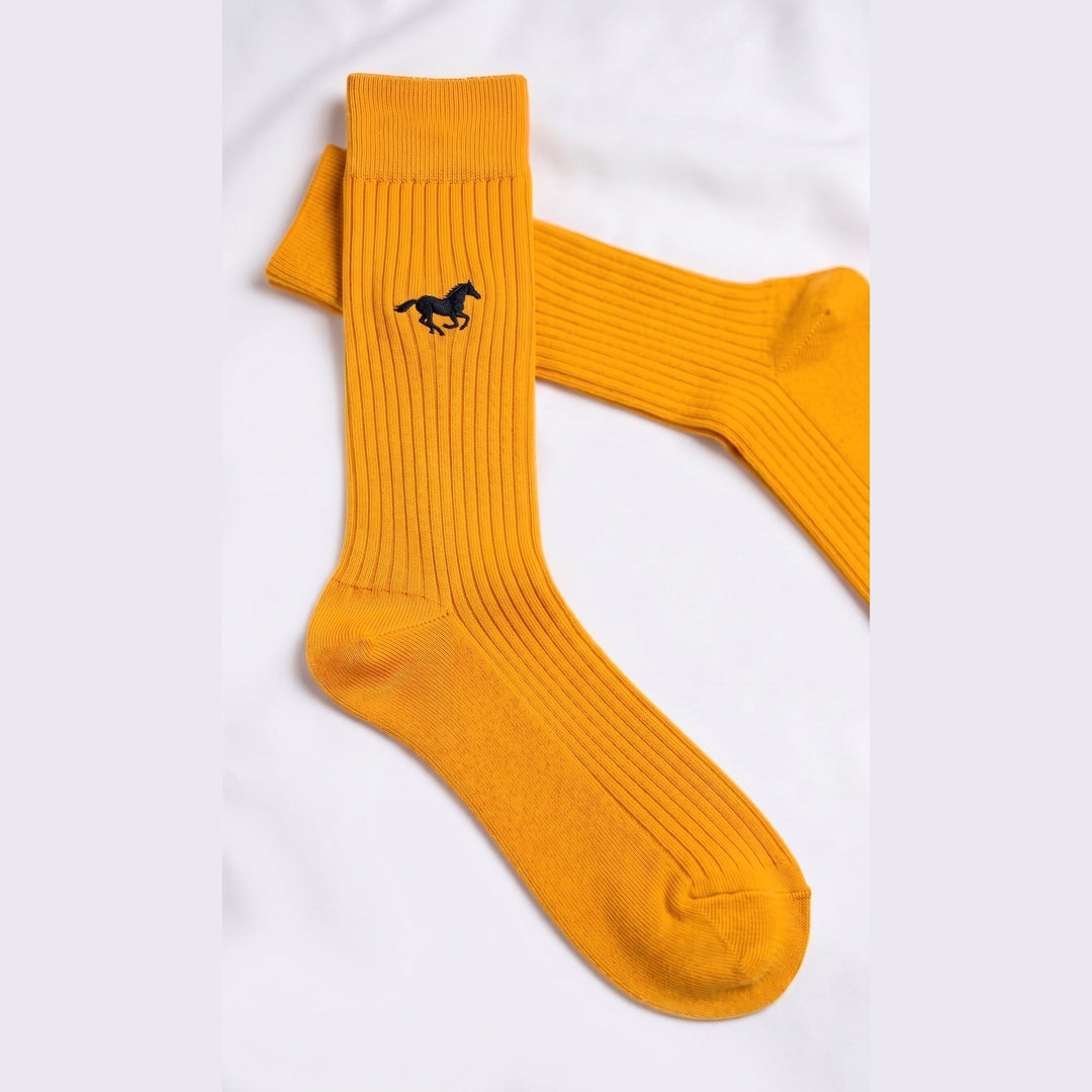 Close-up of mustard ribbed cotton sock showing the small embroidered galloping horse emblem and fine rib knit