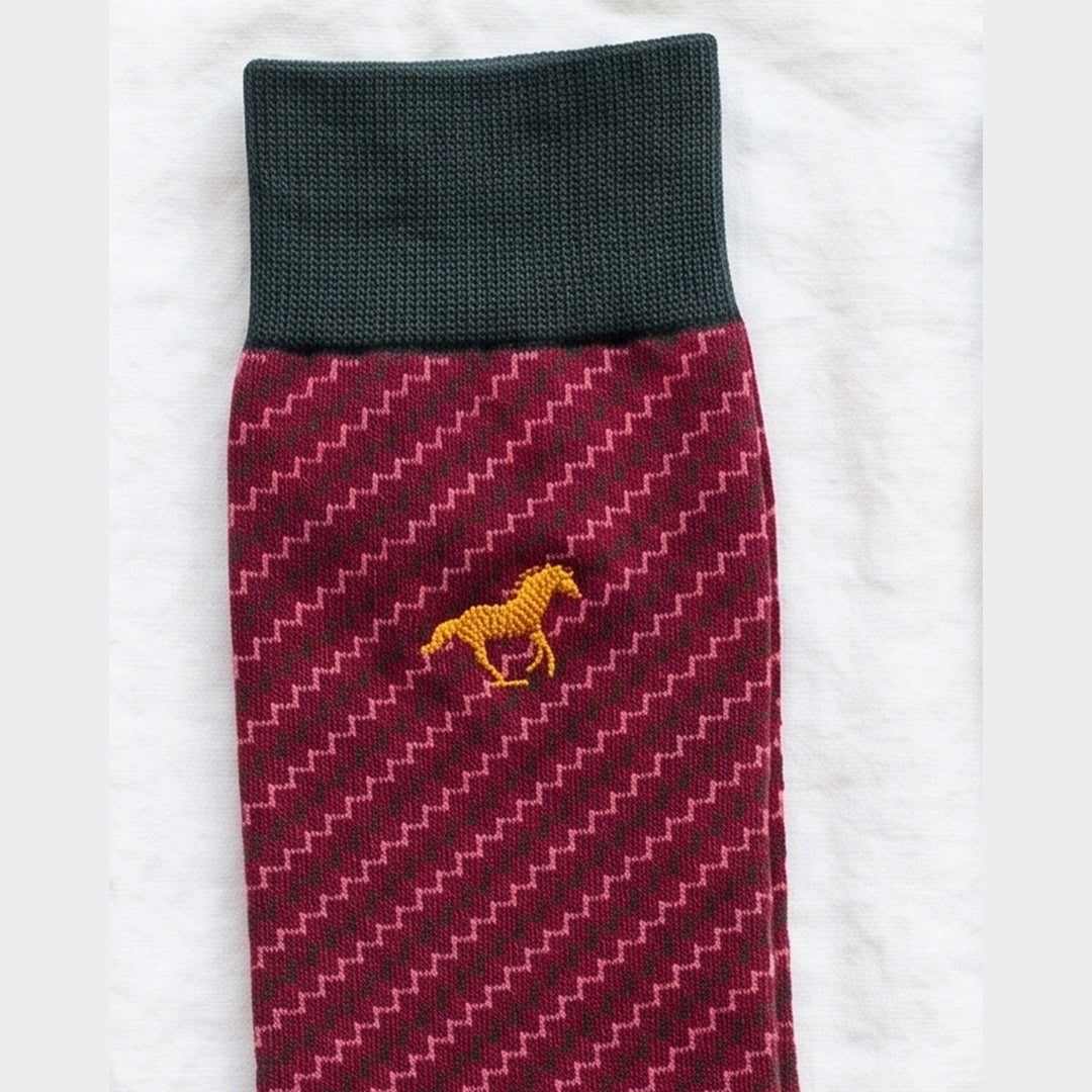 Close-up of burgundy Galloper Zigzag sock with green cuff, diagonal zigzag knit and yellow embroidered horse