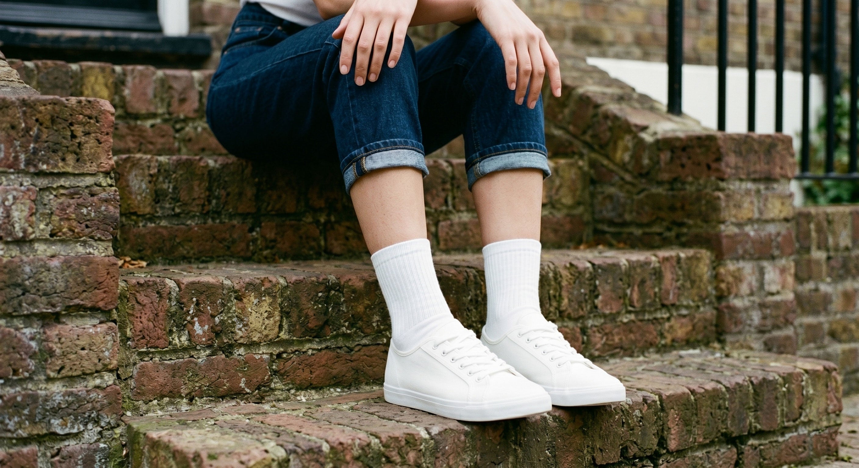 Woman wearing white ribbed cotton crew socks with white trainers sitting on London brick steps, casual street style UK