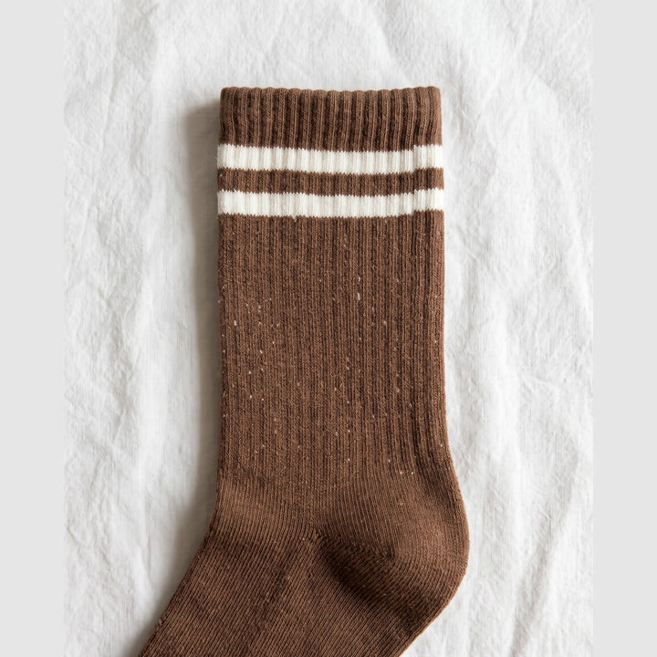 Close-up of brown ribbed tennis sock showing the two cream cuff stripes and flecked cotton knit